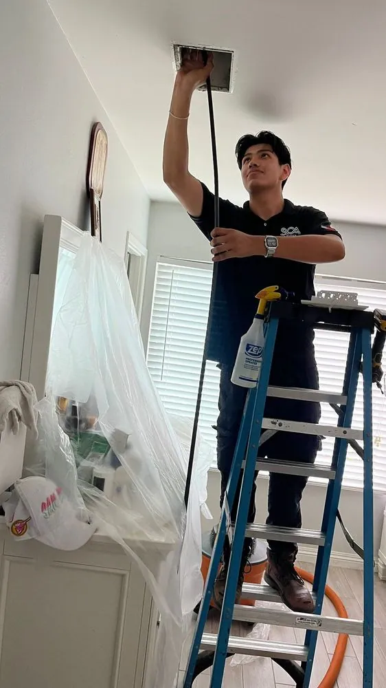 Sky Clean Air technician cleaning a ceiling vent from a ladder